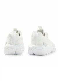 Bílé sportovní boty s texturovaným svrškem, odvážnými, tvarovanými podrážkami a smyčkovými poutky na patě. Hladký povrch a moderní design.