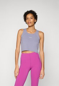 Lila rövidített tank top, lekerekített nyakkivágással, slim fit fazonnal és logó részlettel, magas derékú, élénk rózsaszín jóganadrággal párosítva.