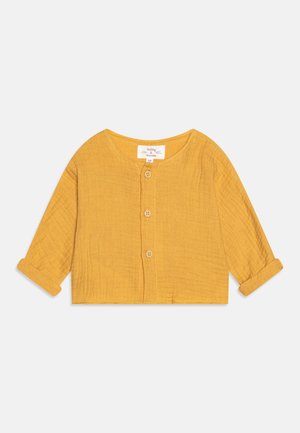 Haut en coton jaune moutarde à manches longues, col rond et fermeture à boutons. Dispose de poignets retroussés et d'un tissu texturé.