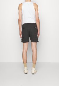 Shorts noirs en matériau doux, dotés d'une taille avec cordon de serrage et de deux poches arrière, associés à un débardeur blanc et des baskets légères.