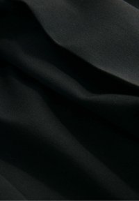 Gros plan d’un tissu noir avec des plis doux et une texture lisse sous un éclairage diffus.