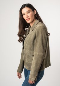 Giacca in suede verde oliva, con chiusura a zip, due tasche frontali e colletto strutturato. Tessuto liscio con un fit moderno.