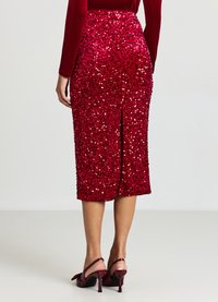 Roter Pailletten-Bleistiftrock mit einem Schlitz auf der Rückseite, mit figurbetontem Schnitt und glänzender Oberfläche. Kombiniert mit roten Slingback-Pumps mit hohem Absatz.