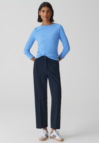 Lichtblauw geribd longsleeve shirt gecombineerd met donkerblauwe, op maat gemaakte broek en witte sneakers met donkerblauwe strepen. Getextureerde stof met een aansluitend ontwerp.