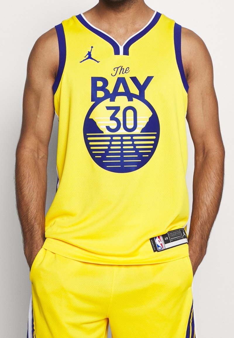 Maillot de sport jaune avec des accents bleus, présentant un graphique circulaire avec le texte "The BAY 30." Fabriqué en tissu en maille, au design décontracté.