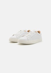 Hvite lær sneakers med tonale snører, beige fôr og en teksturert gummisåle. Har subtile perforeringer og gulløyler.