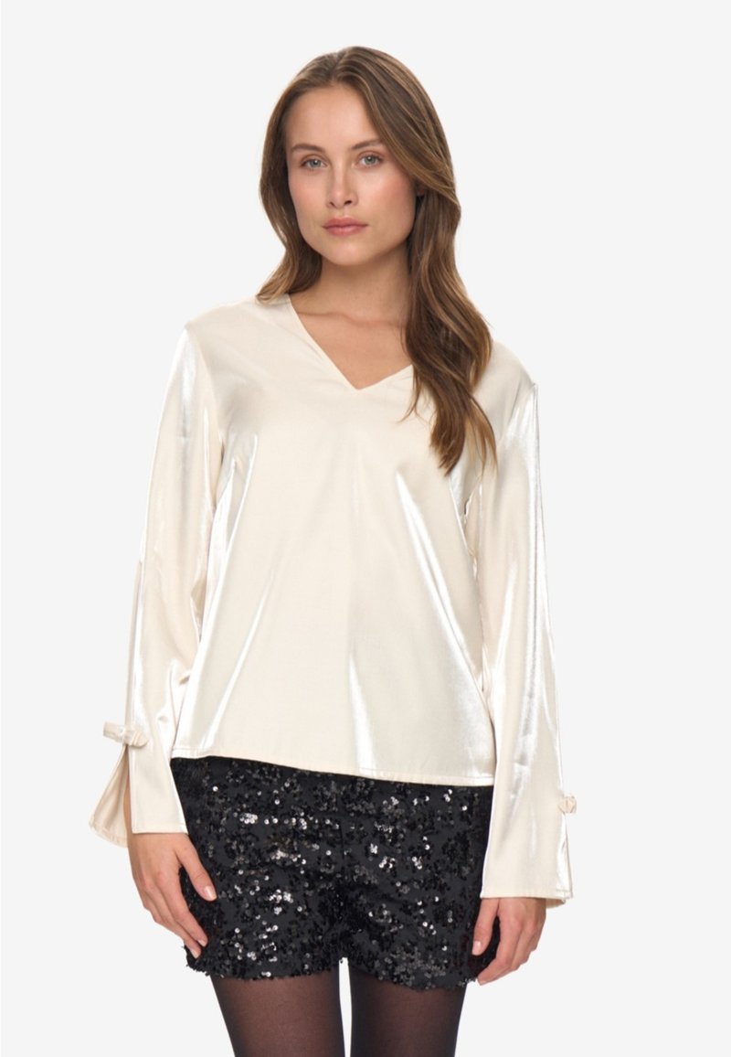 Ivory satin long-sleeve top with a V-neck and bell sleeves. Paired with black sequin shorts. Smooth texture, shiny finish, and relaxed fit.