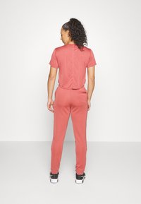 Top desportivo coral de mangas curtas e curto combinado com calças de treino a condizer, com bolsos laterais e punhos elásticos.