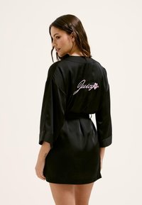 Melnas satīna halāts ar platām piedurknēm un jostasvietā saistītu jostu. Aizmugurē ir rozā izšuvumi ar vārdu "Juicy" un ziedu rotājumiem.