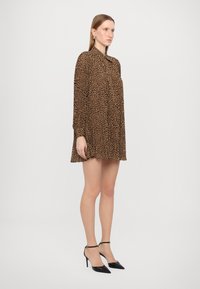 Leopardmönstrad klänning i brunt och svart, med krage och långa ärmar. Modellen matchar den med svarta stilettohögklackade skor och ankelrem.