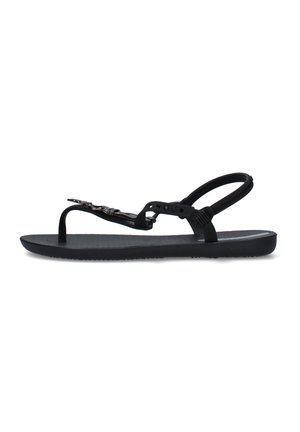 Sandalo nero piatto con cinturino tra le dita, cinturino alla caviglia e dettaglio metallico decorativo sulla parte superiore del piede.