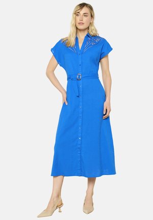 Vestido midi azul con botones y mangas cortas, cinturón en la cintura y detalles bordados en la zona de los hombros. Textura de tela suave.
