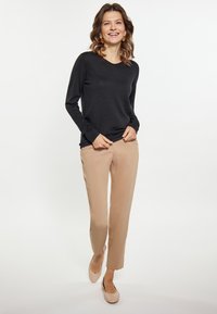 Un top negru cu dungi, cu mâneci lungi, asortat cu pantaloni bej și balerini roz deschis. Modelul are părul brun deschis, ondulat și zâmbește.