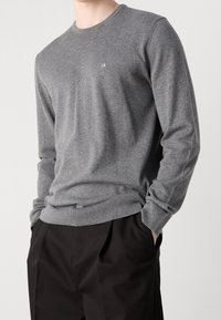 Maglione con scollo rotondo grigio realizzato in un tessuto soffice e strutturato. Logo evidenziato sul petto e polsini e orlo a coste. Abbinato a pantaloni neri.