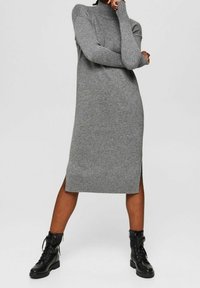 Robe pull en maille grise avec col montant, manches longues, fentes latérales et ourlet côtelé. Associée à des bottes de combat noires à lacets.