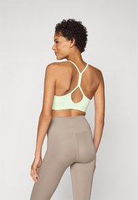 Top desportivo verde-claro com um design cruzado nas costas e detalhe em forma de buraco. Feito de um tecido suave, combinado com leggings bejes de cintura alta.