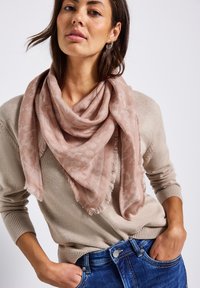 Ljusrosa scarf med texturerat blommönster och fransade kanter, bärs draperad runt halsen, i kombination med en beige tröja och blå jeans.