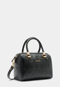 Sac à main en cuir texturé noir avec quincaillerie dorée, accents de logo, doubles poignées supérieures et une bandoulière amovible.