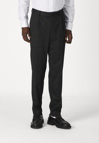 Pantalons à carreaux sombres avec un devant plissé, fabriqués en tissu lisse, avec une coupe fuselée et des coutures détaillées le long des seams.