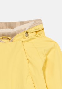 Κίτρινο αδιάβροχο μπουφάν με πλεκτό μπεζ γιακά, διακοσμημένο με λεπτομέρεια με κουμπιά πατιλέτα και λεία εξωτερική υφή, σχεδιασμένο για ζεστασιά και προστασία.