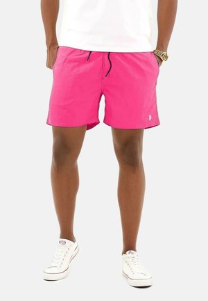 Pinkfarbene Badeshorts mit elastischem Bund, Kordelzug und Seitentaschen, kombiniert mit weißen Sneakers. Gummiertes Logo-Detail auf den Shorts.
