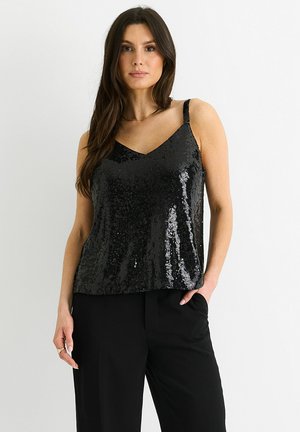 Black sequined camisole with a V-neckline and wide straps, worn with black trousers, features a glossy texture and shimmering detail.