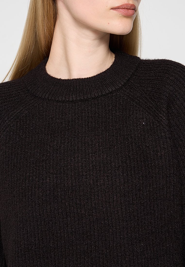 Maglione nero in maglia con una texture a coste, caratterizzato da un colletto rotondo e maniche raglan. Il tessuto appare morbido e caldo.