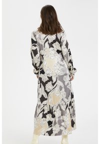 Maxikjol med blommönster i svart, beige och grått. Har lång ärm, ett lager på lager-hem och en slät satinliknande textur.