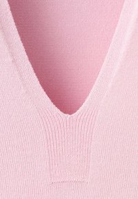 Gros plan d'un tissu tricoté rose avec un décolleté en V profond, montrant des coutures côtelées et texturées détaillées.