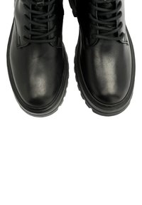 Czarne skórzane botki charakteryzują się gładkim wykończeniem, sznurowanym fasonem, grubą gumową podeszwą i zaokrąglonym noskiem. Brak widocznych wzorów lub dodatkowych zdobień.