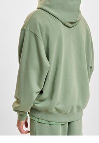 Groene katoenen hoodie met een ruim ontwerp, grote capuchon en ribgebreide manchetten. De achterkant is glad met een relaxte pasvorm en zonder patronen.