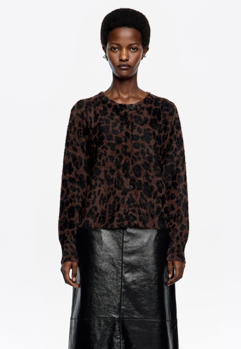 Cárdigan marrón con estampado de leopardo, de textura suave, escote redondeado y botones frontales, combinado con una falda de cuero negra.
