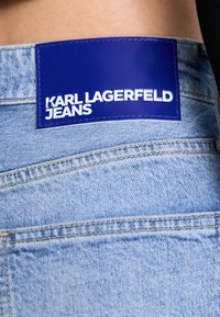 Ljusblå denimjeans med en framträdande blå etikett sydd baktill, som visar "KARL LAGERFELD JEANS" i vit text.
