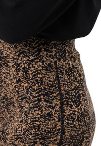 Jupe en tricot présentant un motif abstrait noir, marron et beige, avec une taille haute et une texture lisse, conçue pour une silhouette ajustée.