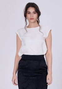 Blouse blanche à manches courtes en tissu léger, associée à une jupe noire texturée avec une taille ajustée.