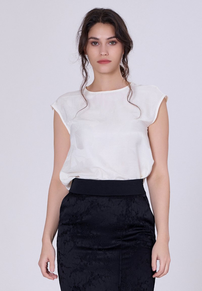 Blouse blanche à manches courtes en tissu léger, associée à une jupe noire texturée avec une taille ajustée.