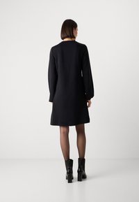 Zwarte lange mouw jurk met een relaxed fit, ronde halslijn en een lengte tot halverwege het bovenbeen, gecombineerd met zwarte enkellaarsjes met blokhakken.