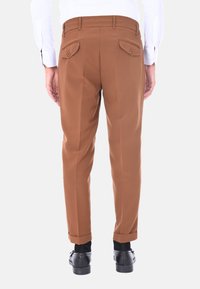 Pantaloni marroni su misura con gamba dritta, orli risvoltati, due tasche posteriori e una texture di tessuto liscia. Indossati con scarpe nere.