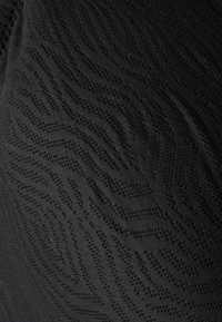 Tecido de malha preto com padrão de onda texturizado e pequenas perforações, criando um design de superfície detalhado.