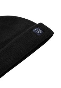 Melnā adīta beanie cepure ar salocītu maliņu, kas ir aprīkota ar mazu tumši zilu etiķeti ar baltu tekstu.