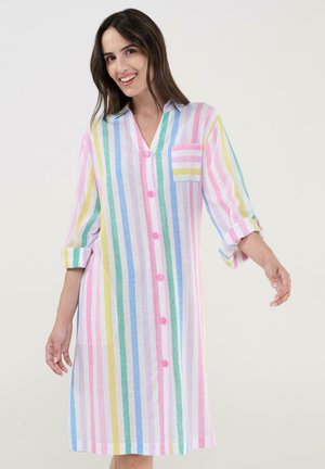 Mujer sonriente, vestida con un vestido de manga larga que llega hasta la rodilla, con rayas verticales en tonos pastel de rosa, azul, verde y amarillo, botones delanteros y un bolsillo en el pecho.