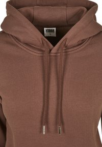 Brun hettegenser med frontlomme, snøring i hetta og myk tekstur. Har et merke inni kragen. Designet er enkelt og funksjonelt.
