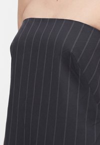 Κοντινό πλάνο ενός ατόμου που φοράει ένα μαύρο τοπ χωρίς τιράντες με λεπτές κάθετες λευκές ρίγες.