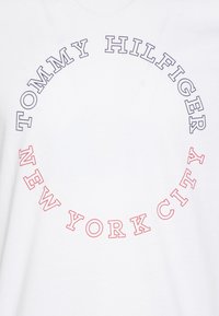 Camiseta de algodón blanca con diseño de texto circular. "TOMMY HILFIGER" en azul y "NEW YORK CITY" en rojo. Estilo simple y casual.