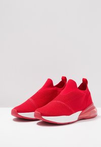 Červené sportovní boty s pleteným svrškem, designem na obouvání a strukturovaným vzorem. Obsahují bílou mezipodešev a průhlednou gumovou podrážku.
