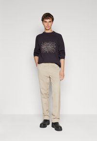 Sudadera negra de manga larga con un diseño de strass "HUGO", combinada con pantalones beiges y zapatos de plataforma negros. Textura suave, ajuste relajado.