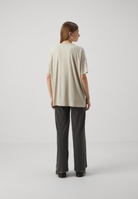 Helebeige suuruse T-särk lühikeste varrukatega, täiendab tumedate hallide triibuliste pükstega, seistes ühetaolisel taustal. Mustad platvormkingad.