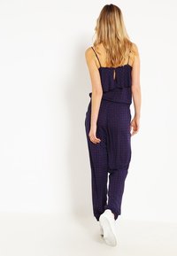 Navy jumpsuit med volangtop, prydd med ett blommönster i röd och vit. Designen inkluderar justerbara axelband och elastisk midja.