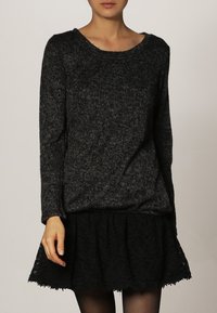 Svart stickad tröja med ribbad struktur och bred rundad halsringning, i kombination med en svart utsvängd kjol med spetsdetaljer.