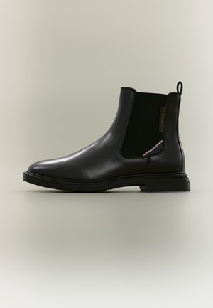 Bottine Chelsea en cuir noir avec panneau latéral élastique, languette au talon et semelle en caoutchouc basse.